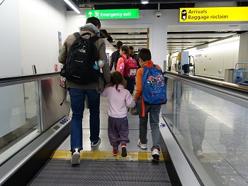 Air travellers walk on a moving walkway through airport. Credit: istock.com/Akabei