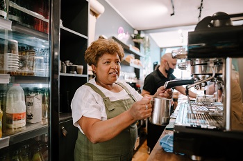 Older woman at work in cafe. Credit: Ageing Better image library
